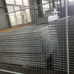 A large stack of galvanized temporary fencing panels with welded mesh, stored indoors in a warehouse, demonstrating inventory ready for dispatch.