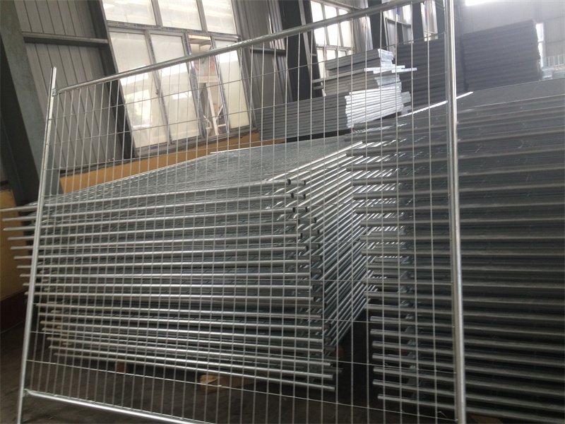 A large stack of galvanized temporary fencing panels with welded mesh, stored indoors in a warehouse, demonstrating inventory ready for dispatch.