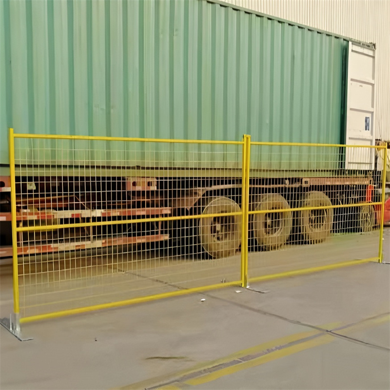 Yellow temporary fence panels with flat bases are set up on a paved surface, running in front of a large green shipping container on a truck.