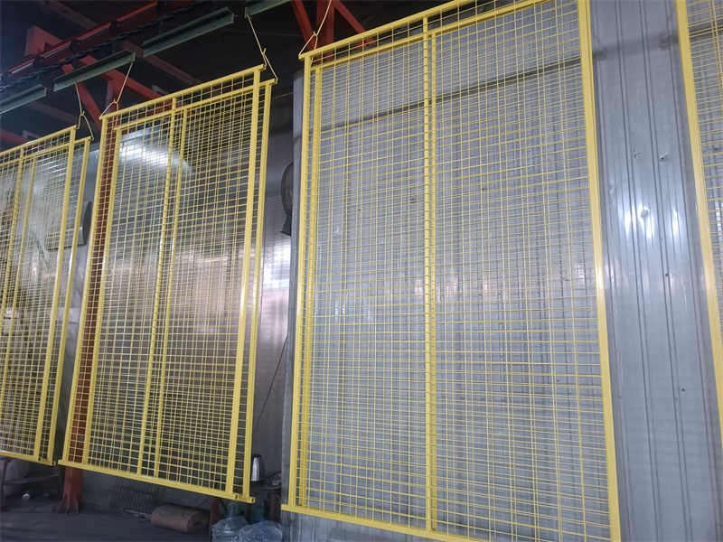 Several yellow mesh temporary fence panels are shown hanging on a production line or rack, likely after a coating process, displaying their grid structure and bright color.