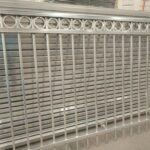 Stack of new galvanized steel picket fence panels with a decorative circular top rail design, ready for installation.