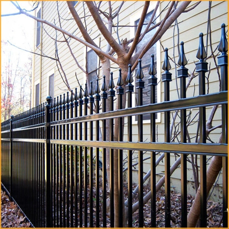 A black ornamental steel fence with decorative finials installed in front of a house with beige siding and a bare tree.
