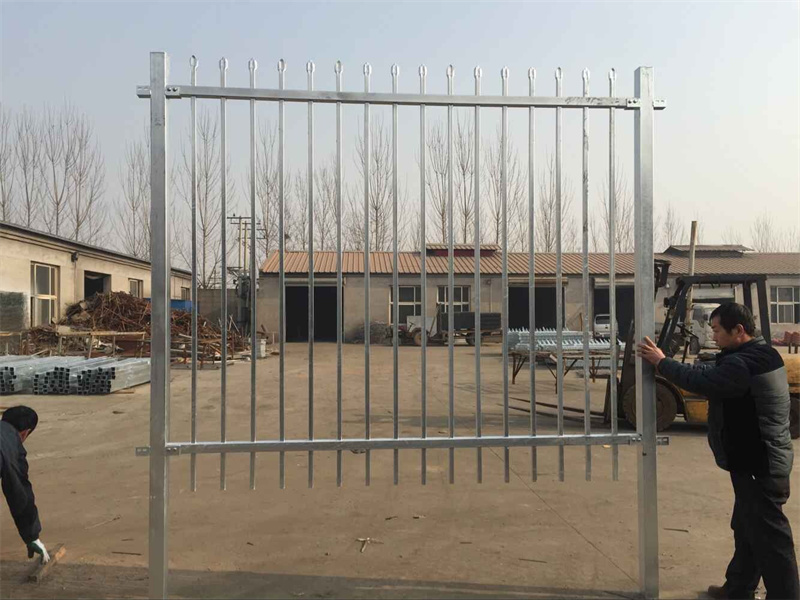 Two workers hold up a large, hot-dip galvanized steel fence panel before the final coating is applied.