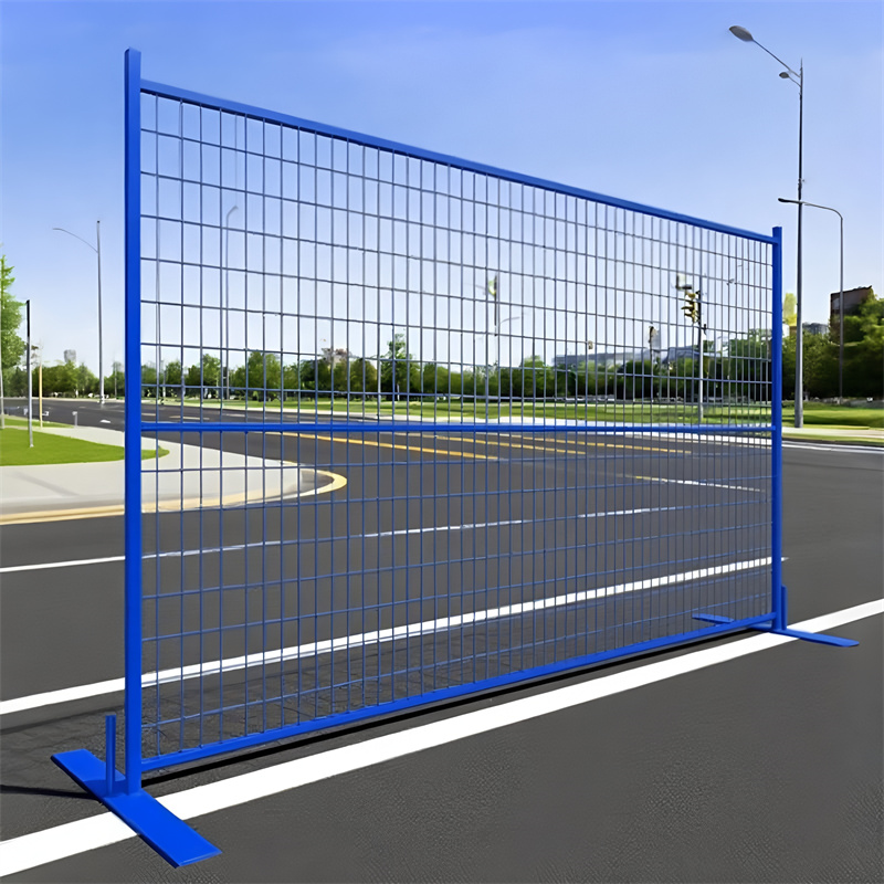 A single blue temporary welded wire mesh fence panel with flat bases, standing on a paved road with a curb and green space in the background.