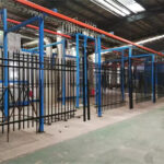 An automated production line with black powder-coated steel fence panels moving through a factory.
