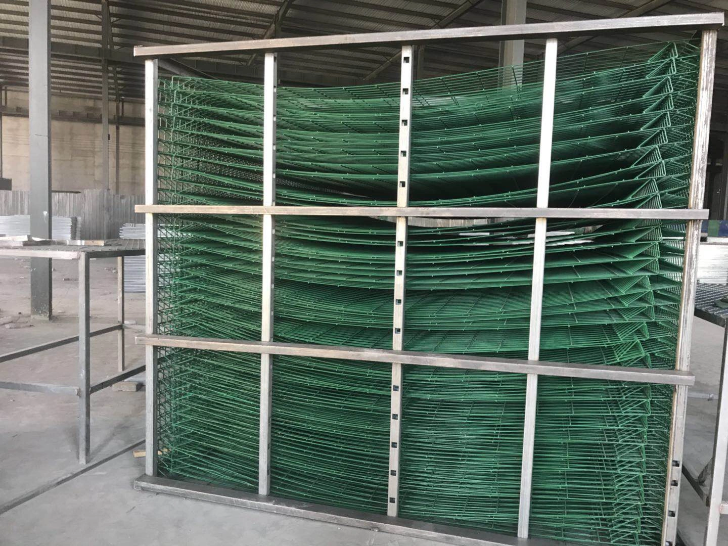 Stack of green BRC fence wire mesh panels stored in a metal rack inside DB Fencing's warehouse, showcasing their manufacturing capacity and durable, compliant fencing products for construction, event management, and agricultural use.