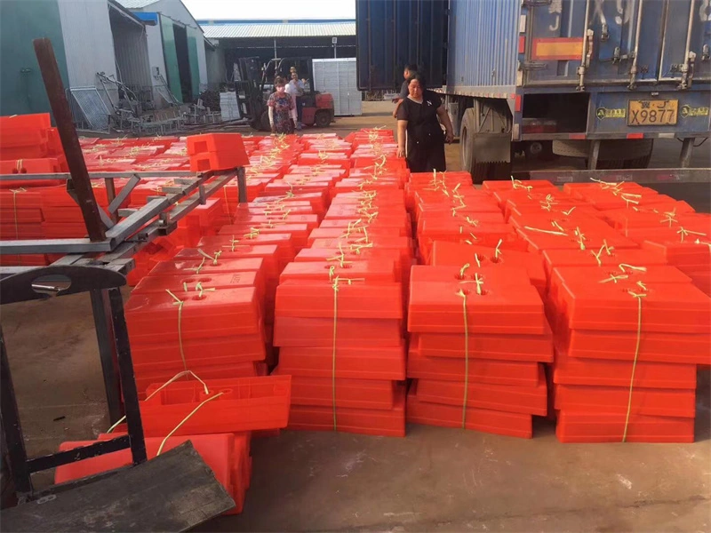 Red plastic feet for temporary fences, manufactured by DB Fencing (Anping Deban Metal Wire Mesh Products Co., Ltd), stacked in a factory yard with a container truck, highlighting the company's specialized plastic feet production and export-ready inventory for global markets like Australia and New Zealand.
