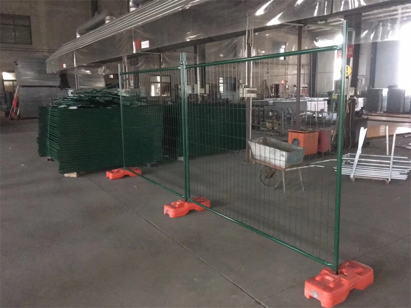 Green temporary fence with orange plastic feet manufactured by DB Fencing, displayed in their Anping warehouse alongside stacked panels, showcasing their production capacity and specialized plastic feet technology.