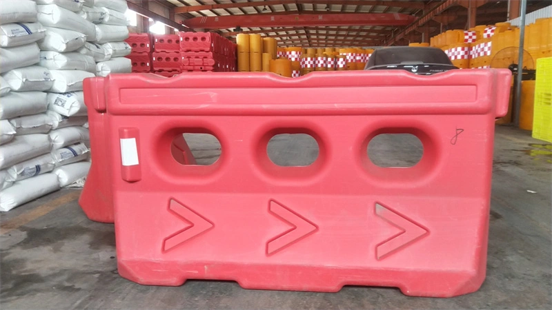 A red plastic temporary crowd control barrier with three oval cutouts and arrow designs, manufactured by DB Fencing, displayed in a warehouse setting alongside construction materials, highlighting the company's one-stop wire mesh and temporary fencing solutions.