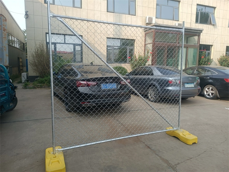 A temporary chain-link fence with galvanized steel mesh and yellow plastic feet, manufactured by DB Fencing, installed in a parking lot to showcase real-world application for construction or event security.