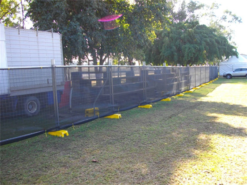 DB Fencing's temporary fence featuring black galvanized mesh and yellow plastic feet installed on a grassy outdoor site, demonstrating its use for event crowd control and construction site security, manufactured by Anping Deban Metal Wire Mesh Products Co., Ltd.