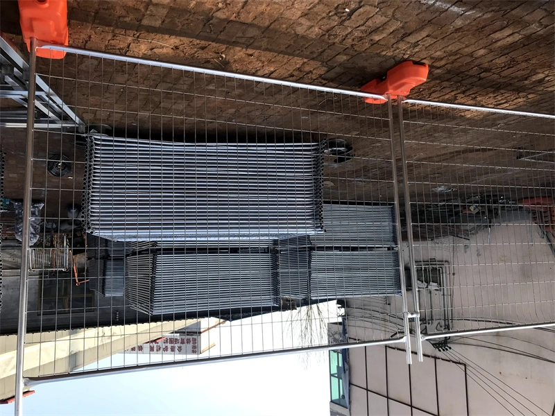 Stacked galvanized temporary fence panels with orange plastic feet, manufactured by DB Fencing, designed for construction sites and eventsideal for construction firms and event managers, with hot-dipped galvanized finish for outdoor durability.