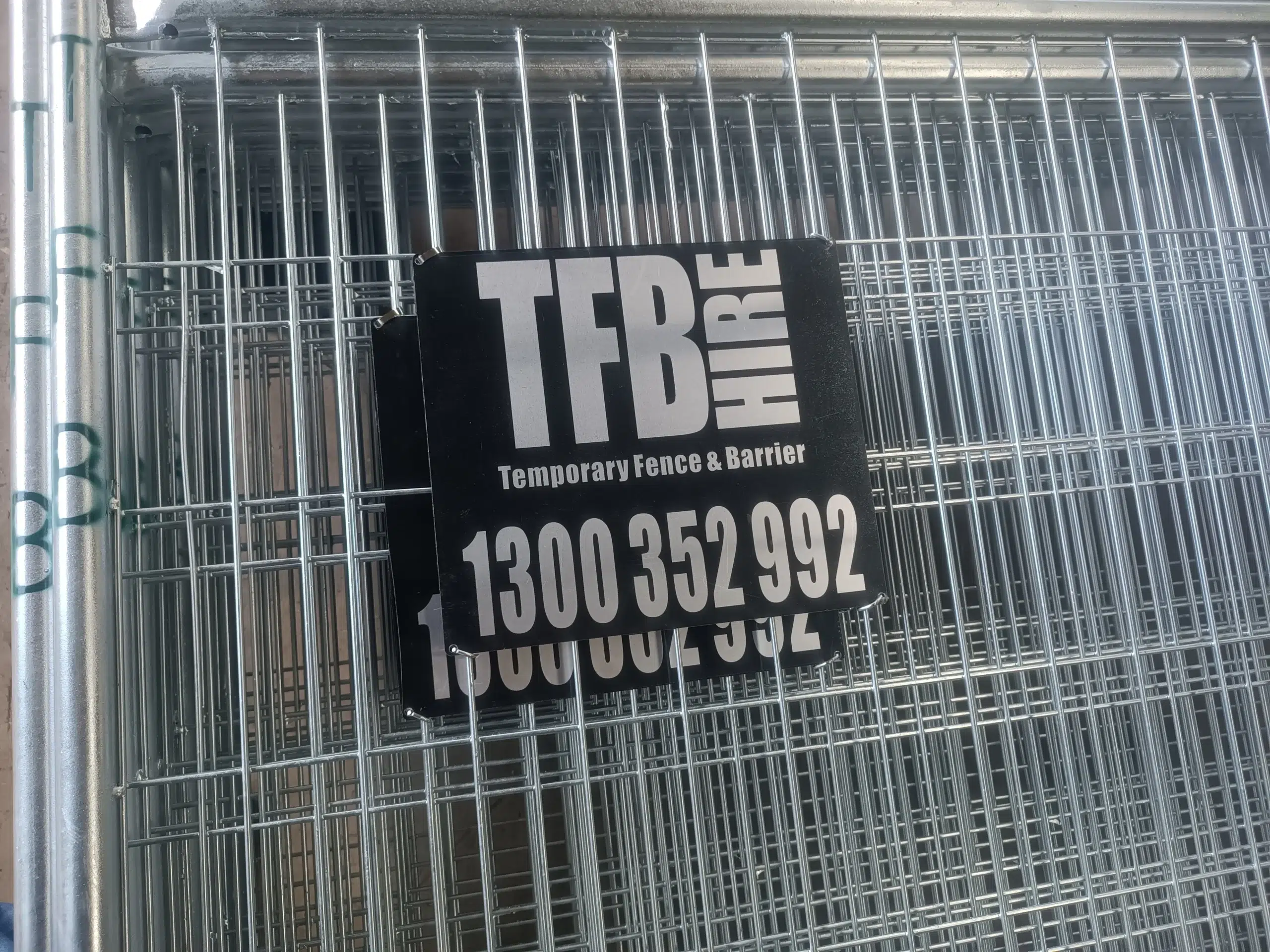 This image features stacked hot-dipped galvanized temporary fencing panels from DB Fencing, bearing a 'Temporary Fence & Barrier' sign with an Australian 1300 number. These durable temporary fencing systems for construction sites are designed for bulk supply to B2B clients, meeting AS 4687 standards for reliable perimeter security in harsh outdoor environments.