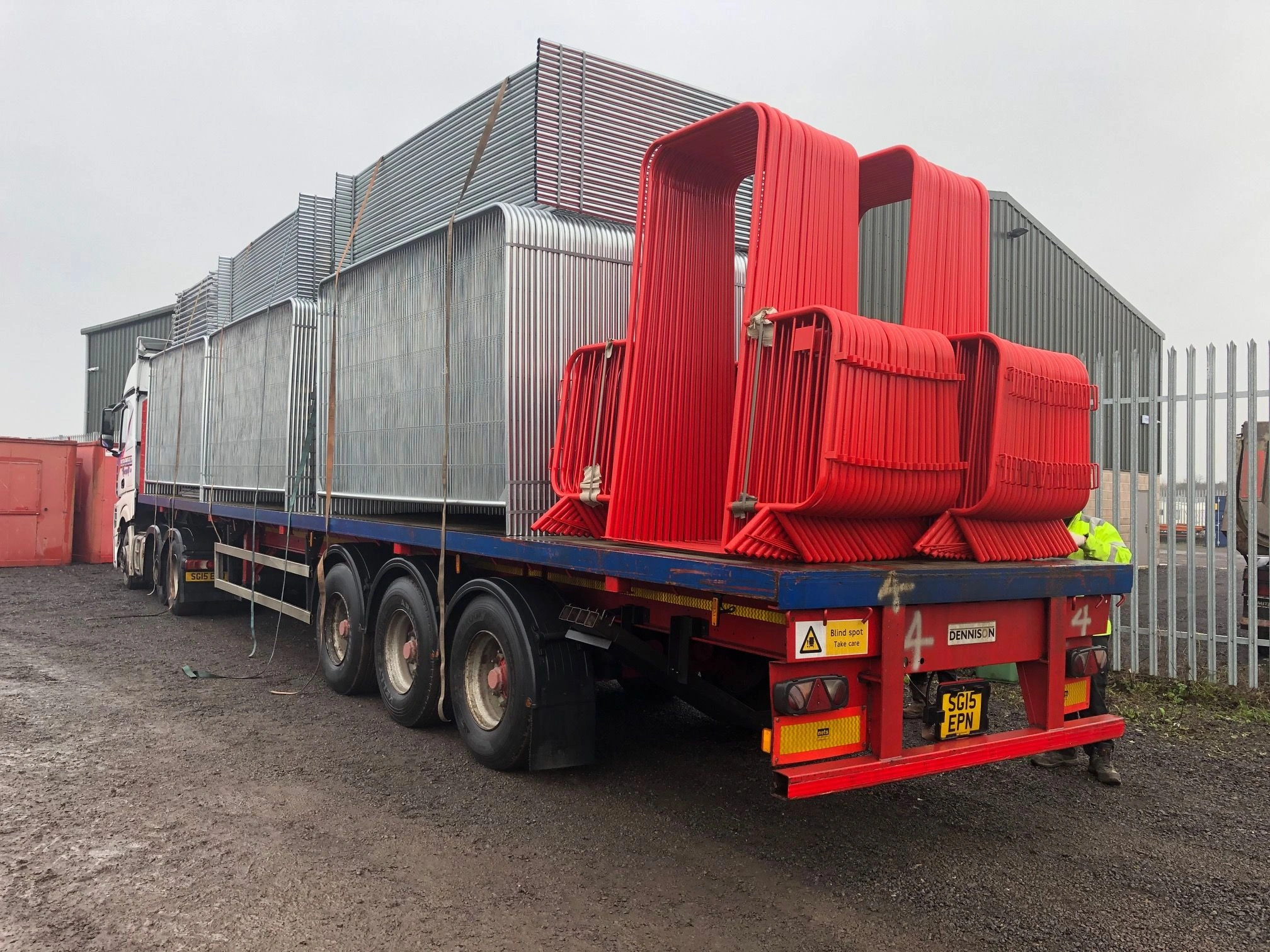 A flatbed truck from DB Fencing, the leading Anping manufacturer, loaded with a large bulk order of bright red Crowd Control Barriers & Event Perimeter Management systems, alongside stacks of galvanized temporary fencing panels. This image showcases our robust production and export capabilities for B2B customers, including event management companies and global distributors, seeking ISO9001/SGS certified solutions.