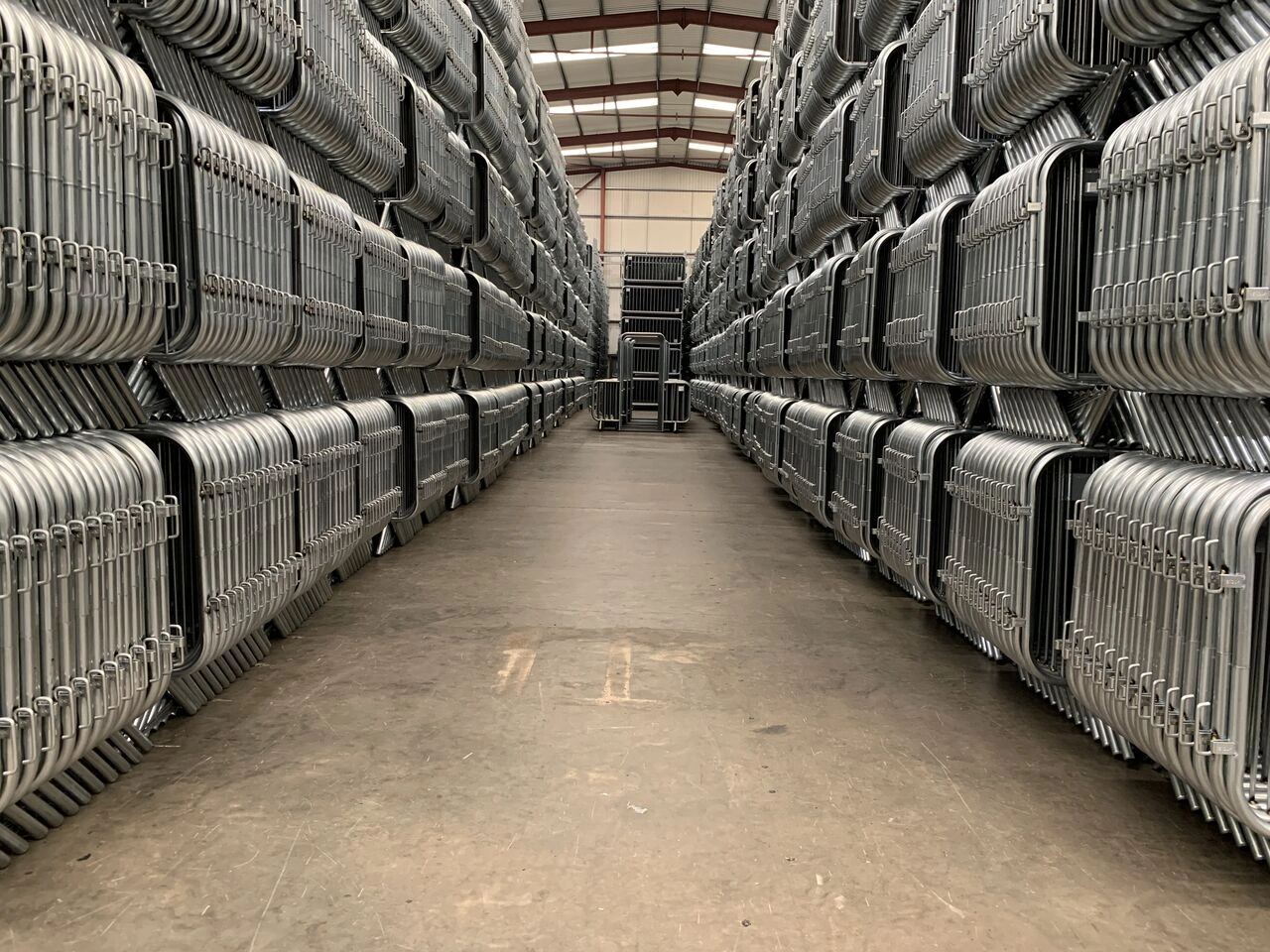 An expansive warehouse at Anping Deban Metal Wire Mesh Products Co., Ltd (DB Fencing) filled with vast stacks of hot-dipped galvanized Crowd Control Barriers for Events & Public Safety. This image demonstrates DB Fencing's significant production capacity and ready bulk inventory for event management companies and global fence distributors.