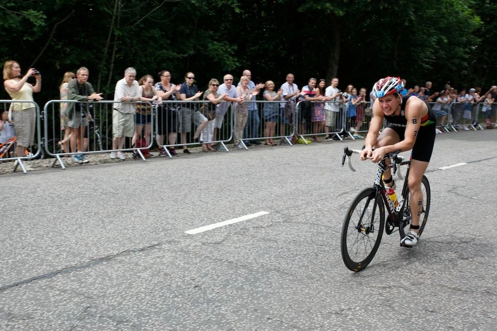 A female cyclist passes spectators safely positioned behind robust DB Fencing crowd control barriers during an outdoor race. These durable metal barriers, part of our 'Crowd Control Barriers for Events & Public Safety' product line, effectively manage crowds and ensure a secure environment.
