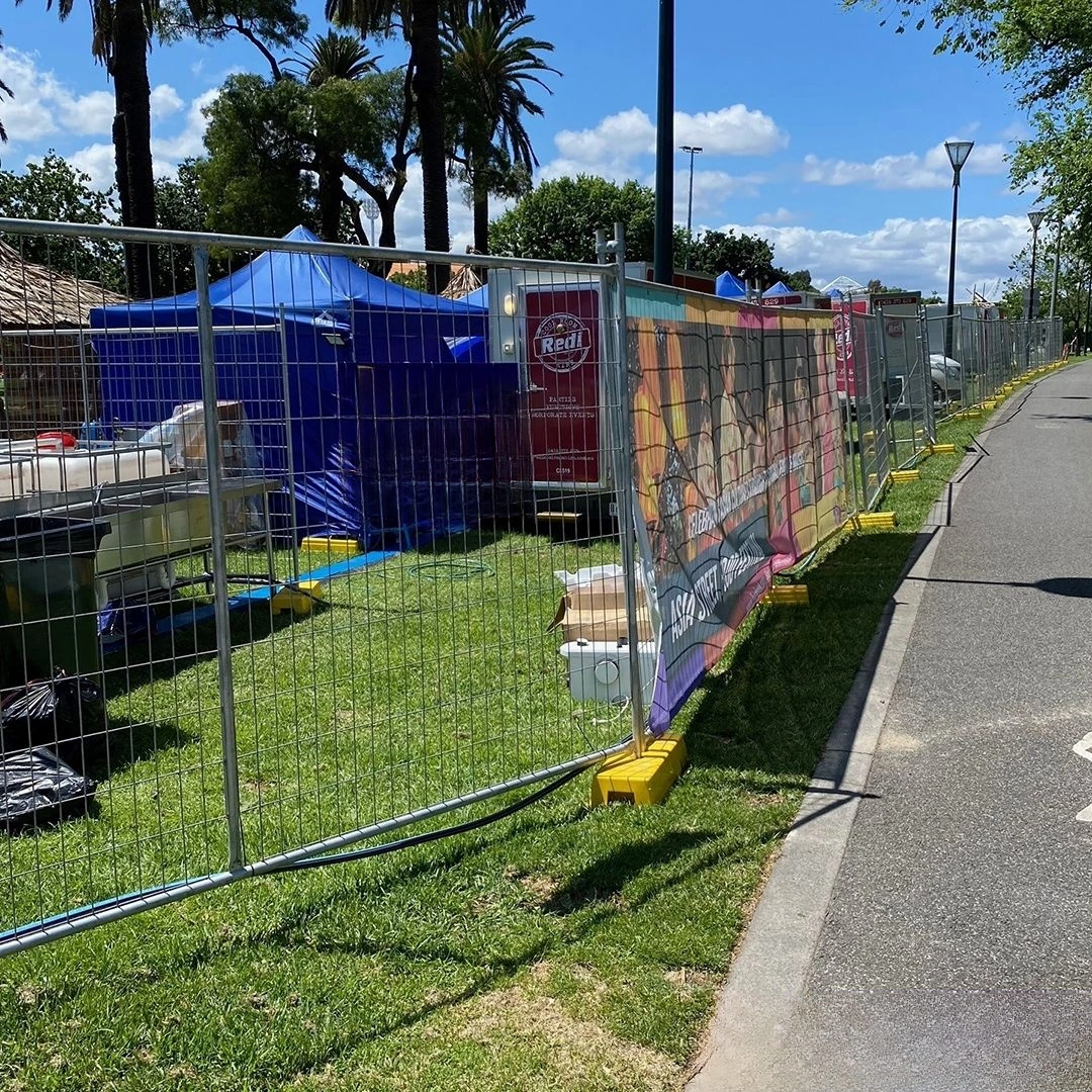 A long line of DB Fencing's temporary crowd control barriers secures an outdoor event site, featuring galvanized fence panels supported by our signature yellow plastic feet. This robust system provides essential public safety and perimeter management for festivals and gatherings, demonstrating DB Fencing's compliant temporary fencing solutions for event management companies.