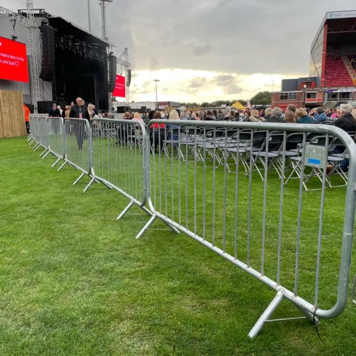 Rows of DB Fencing's galvanized steel crowd control barriers for events & public safety are strategically deployed across a grassy outdoor venue, separating the audience from a stage. These durable barriers provide essential perimeter management and crowd flow control for event management companies, reflecting our commitment to safety and quality.