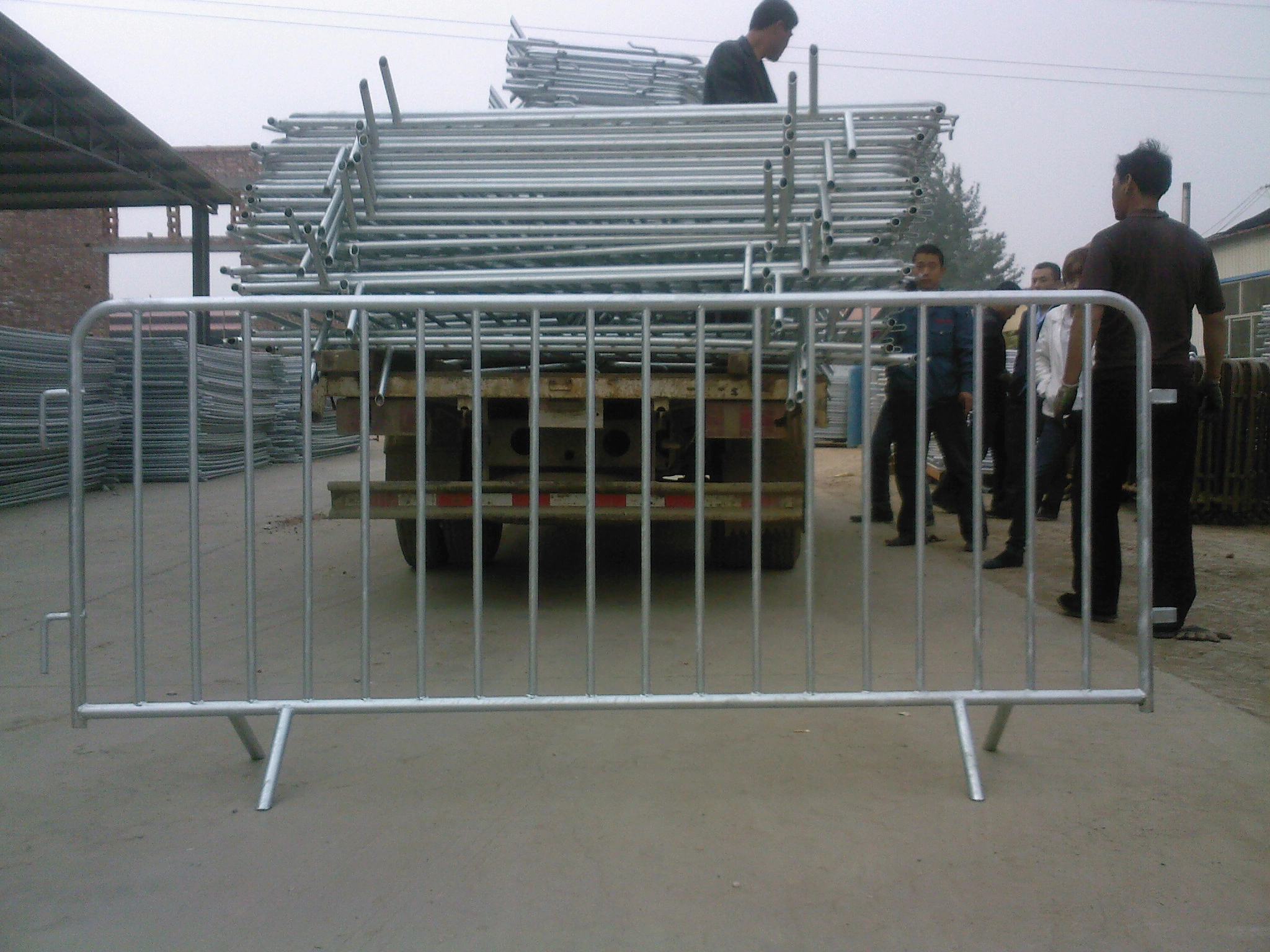 A prominent view of DB Fencing's robust galvanized steel crowd control barriers, with a truck in the background heavily loaded with more barriers, signifying large-scale production. This image showcases our Anping facility's capability to manufacture and export high-quality crowd control barriers, ideal for event management companies and global fence distributors seeking durable, compliant solutions.