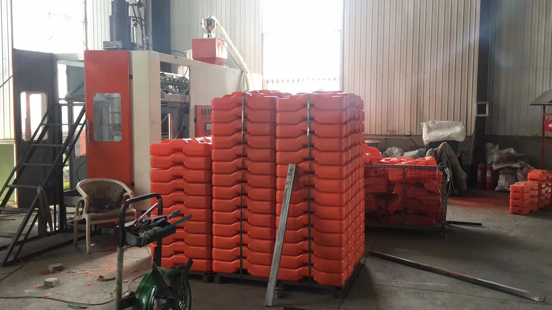 An inside view of DB Fencing's advanced factory floor, showcasing the production of bright orange plastic temporary fence feet and base systems using a specialized molding machine. This image highlights DB Fencing's unique manufacturing capability as the sole supplier in Anping with its own plastic feet machine, ensuring high-quality and compliant temporary fence accessories for global export.