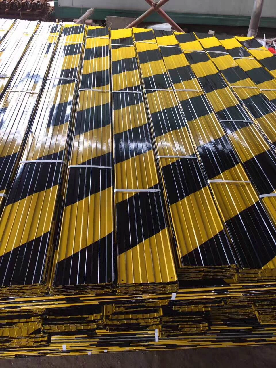 A large stack of newly manufactured steel crowd control barriers, featuring prominent black and yellow diagonal stripes for high visibility and safety. These durable, hot-dipped galvanized barriers from DB Fencing are designed for effective event perimeter management and public safety, meeting compliance standards for global export.