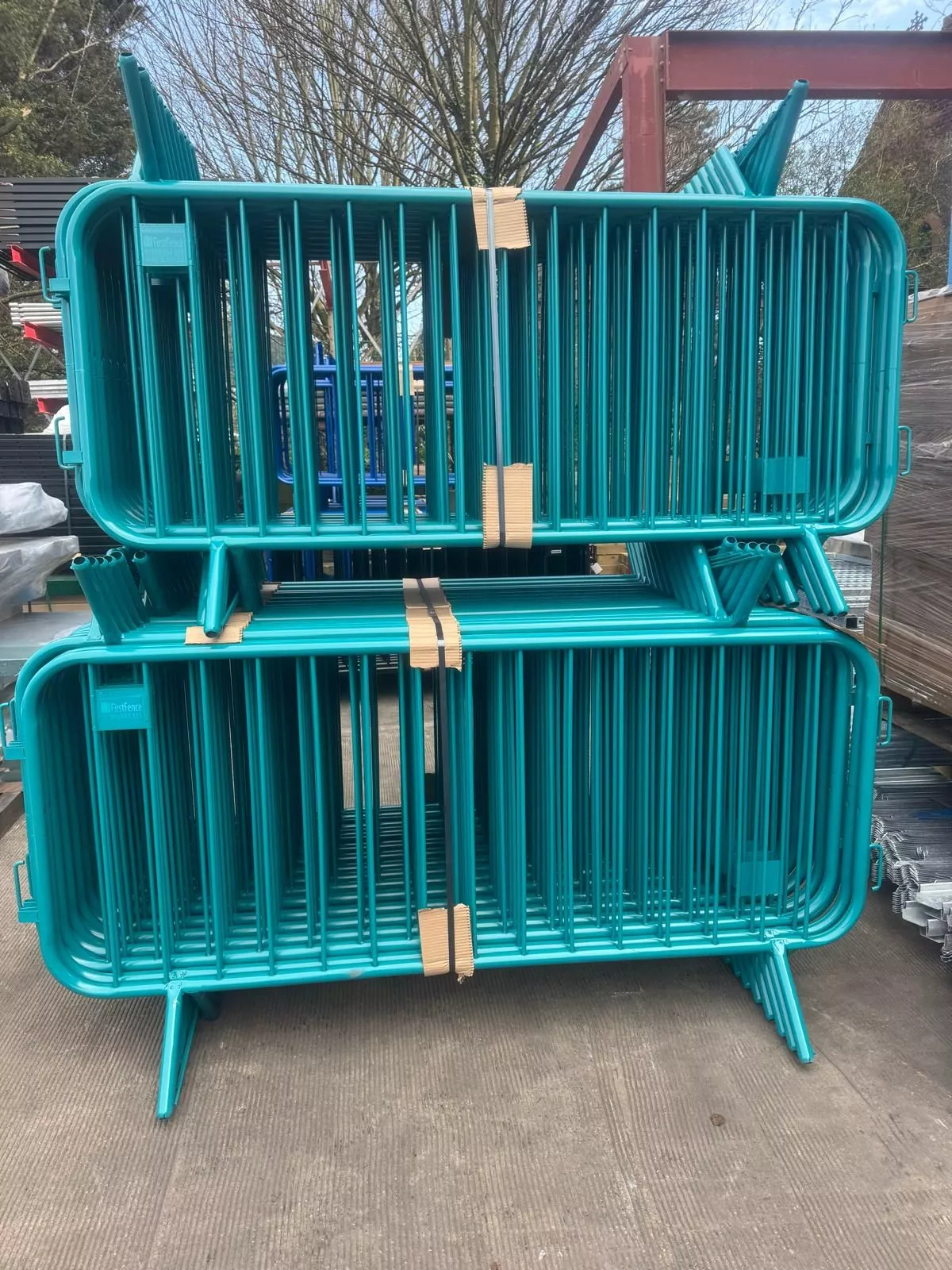 Two stacks of vibrant teal powder-coated DB Fencing crowd control barriers, branded 'Metalfence' and featuring a durable steel construction for effective event perimeter management, are showcased. These robust barriers exemplify DB Fencing's high-quality, factory-direct solutions designed to meet B2B industry standards for crowd control and temporary site security.
