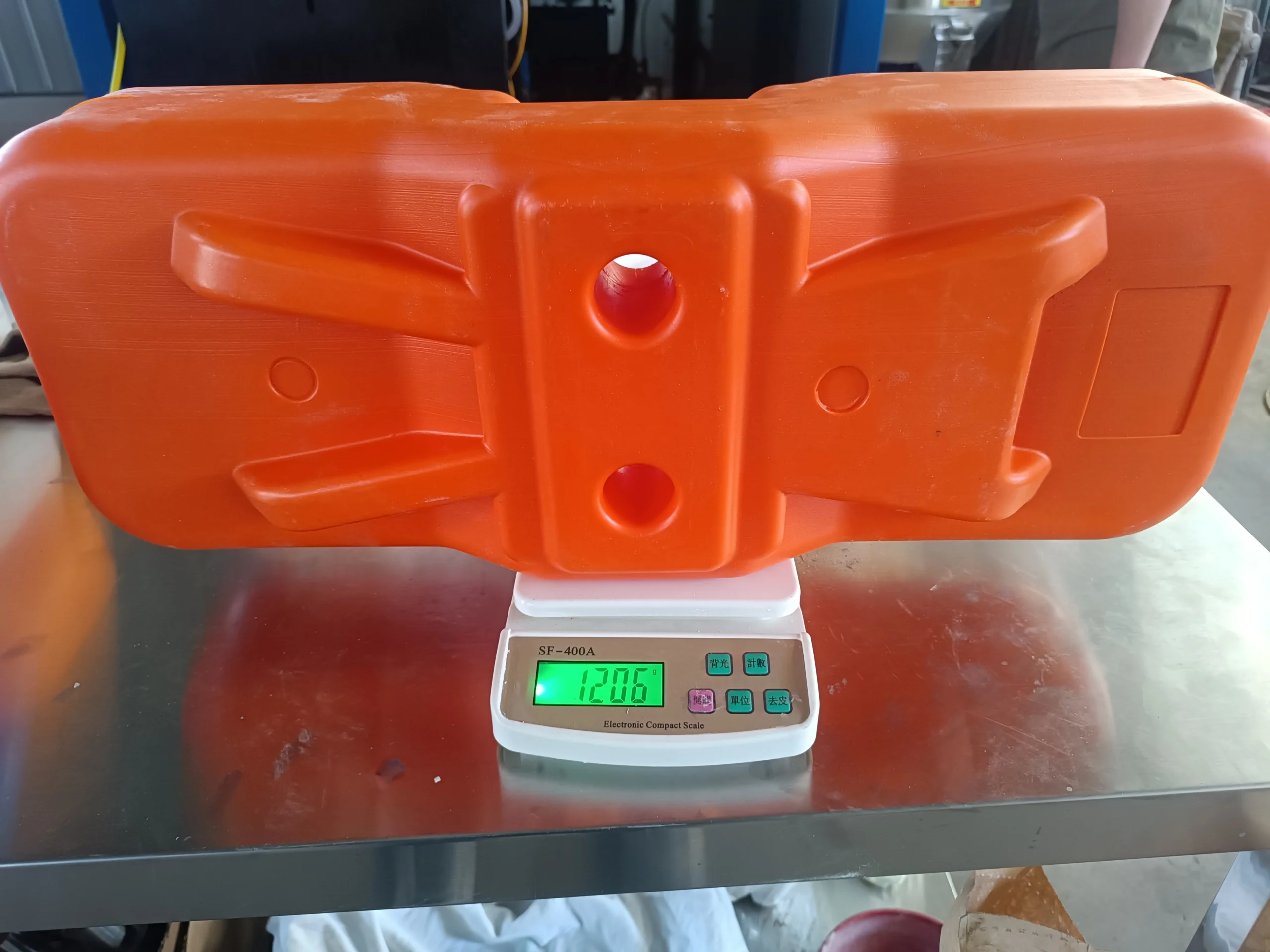 A robust orange plastic temporary fence feet & base system is shown on a digital scale, displaying a weight of 12.05kg. This image from DB Fencing's production line demonstrates our manufacturing expertise and quality control for essential temporary fence feet & base systems, ensuring compliance and durability for our B2B clients in markets like Australia and New Zealand.