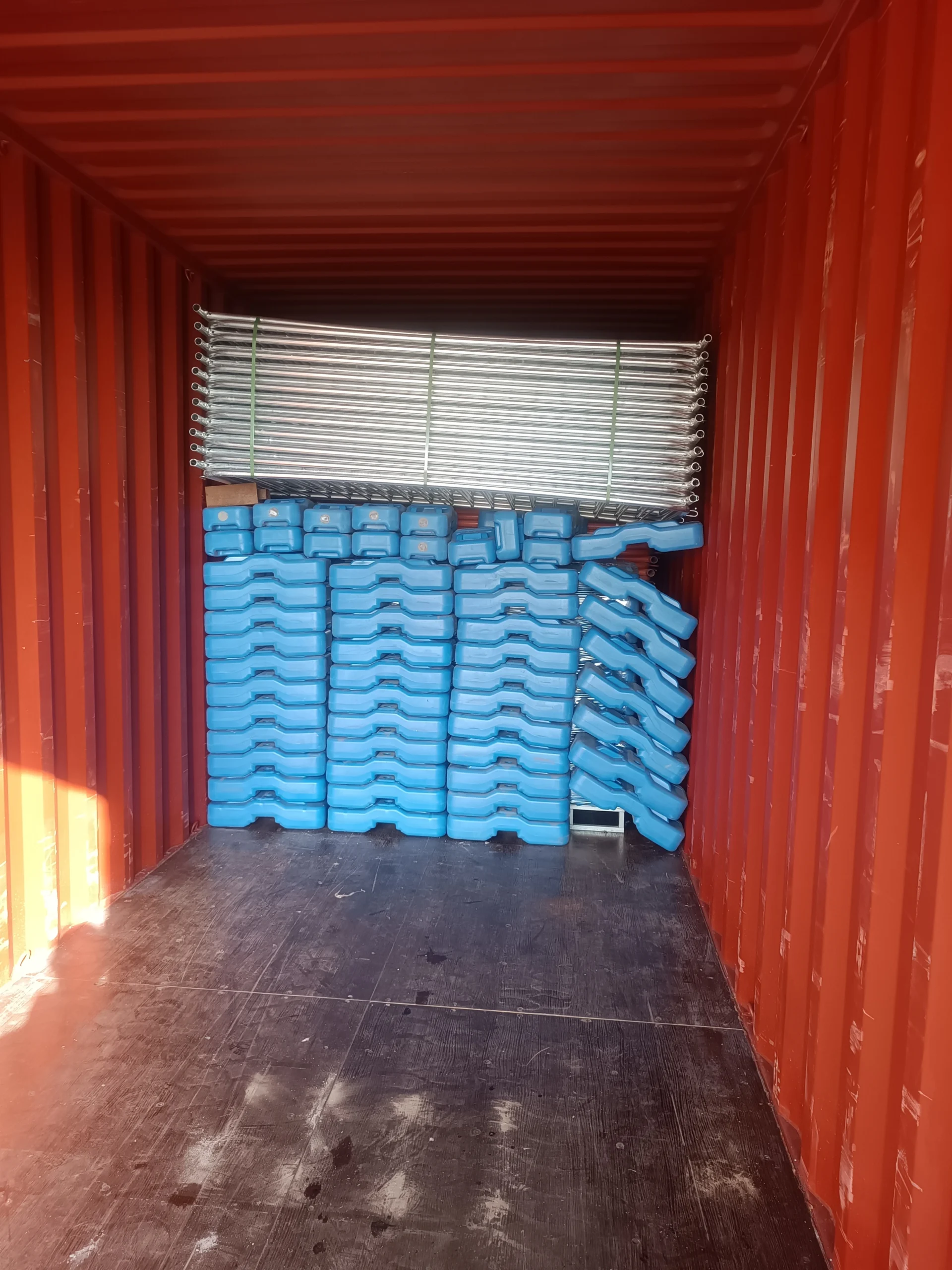 Inside a shipping container, stacked blue DB Fencing Temporary Fence Feet & Base Systems are visible with bundled hot-dipped galvanized temporary fencing components. This scene highlights our efficient export logistics, delivering compliant and durable temporary fencing solutions globally from our own plastic feet machine production.