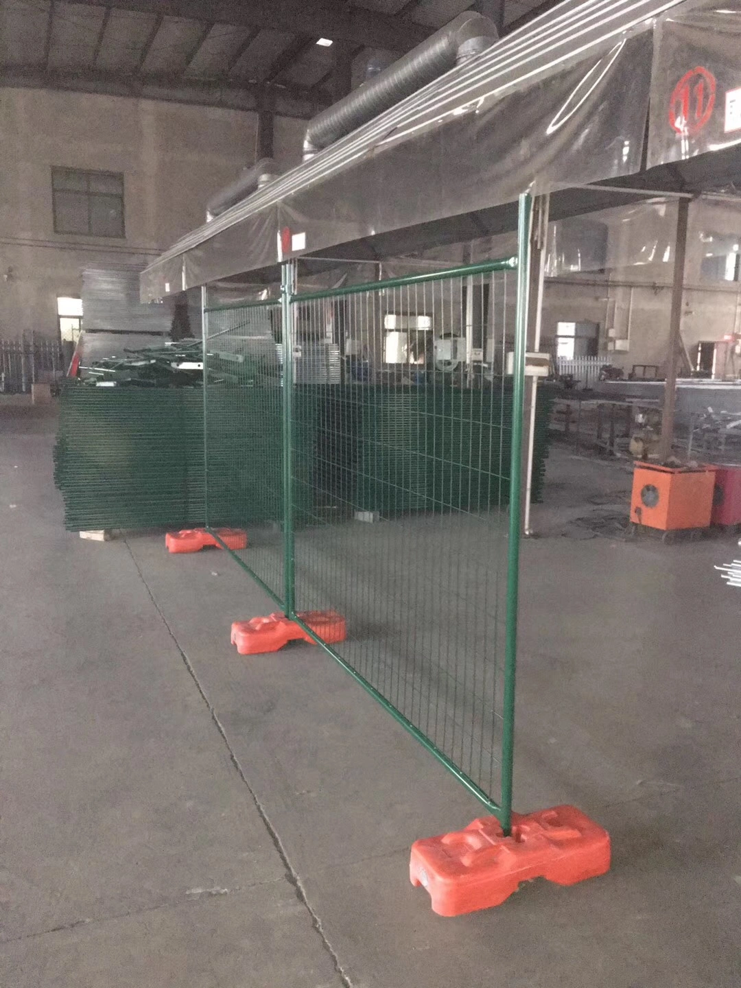 A view inside DB Fencing's Anping factory, showcasing multiple green temporary fence panels firmly supported by our proprietary orange plastic feet base systems. This illustrates our expertise as a leading one-stop manufacturer of high-quality temporary fencing systems and essential temporary fence feet components for construction and event applications.