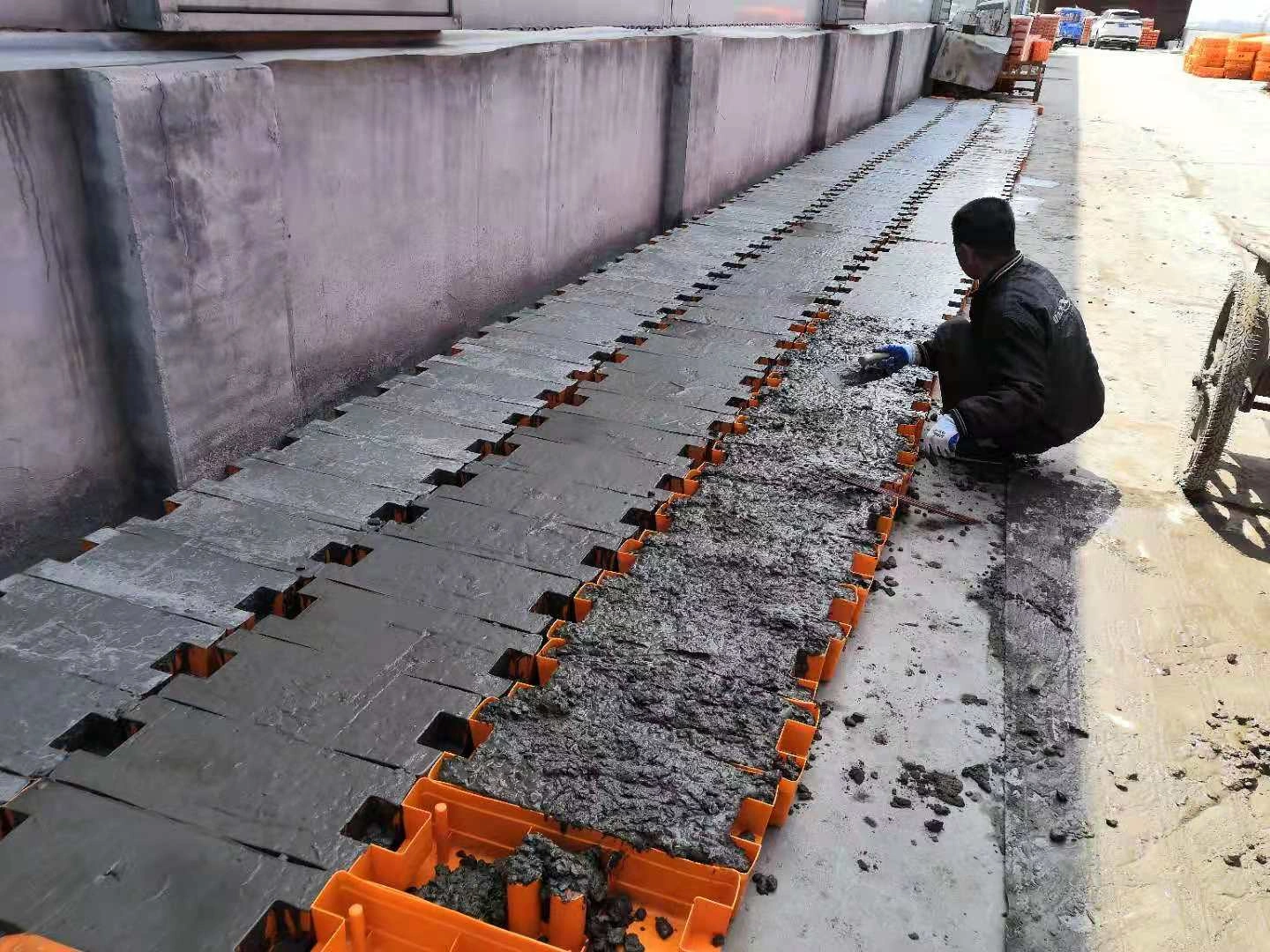 A DB Fencing worker skillfully fills orange plastic molds with concrete, demonstrating our robust in-house manufacturing process for high-quality temporary fence feet & base systems. This showcases our unique capability as the only Anping supplier with our own plastic feet machine, ensuring durable and compliant products for our B2B clients globally.