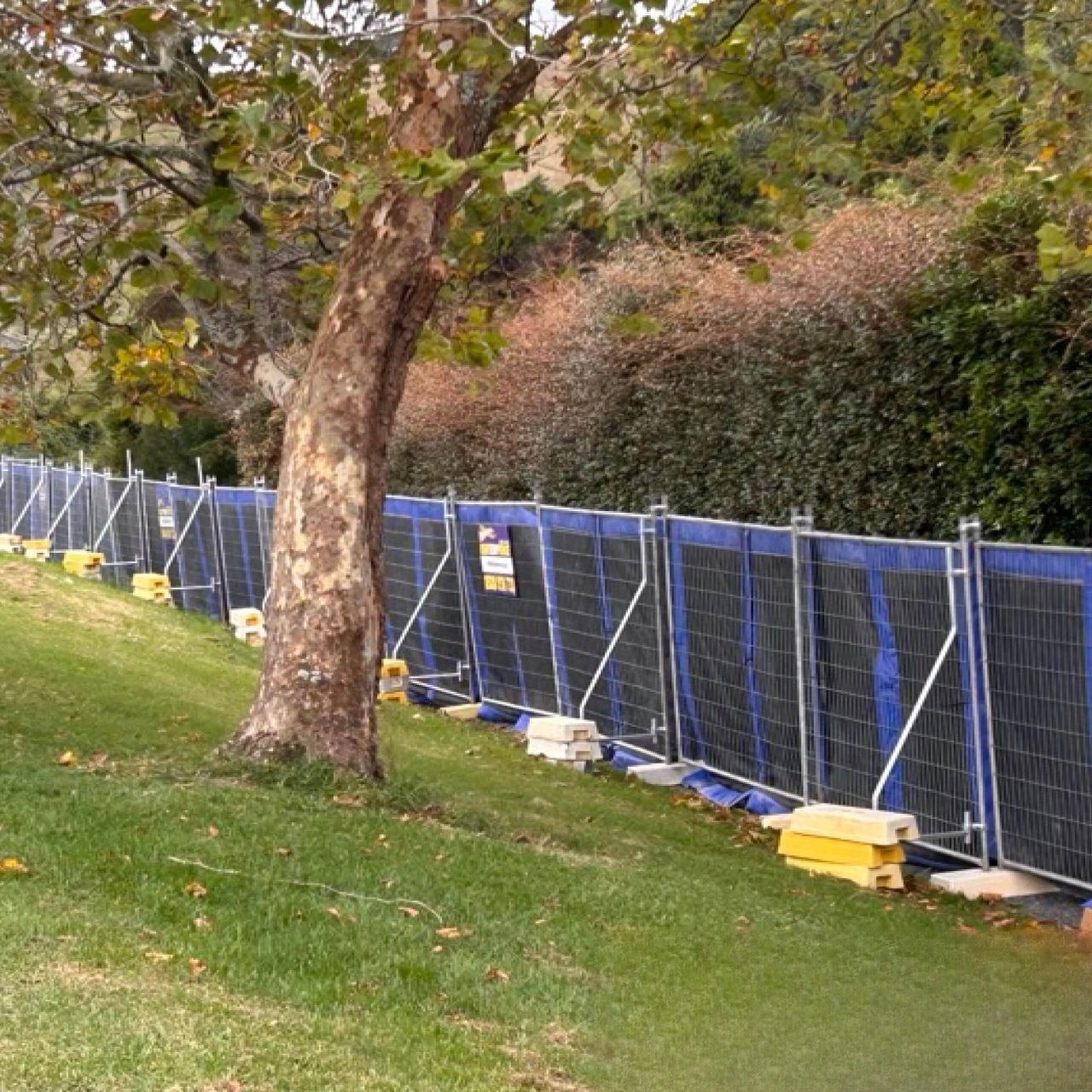 A comprehensive view of DB Fencing's Temporary Fencing Systems for Construction Sites, showcasing sturdy mesh panels with blue screening and robust Temporary Fence Feet & Base Systems securing a perimeter on a grassy incline. These AS 4687 compliant barriers are ideal for civil engineering firms requiring reliable site security.