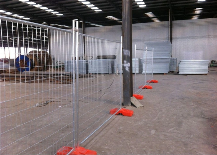 A long line of hot-dipped galvanized temporary fencing panels securely stands on robust orange plastic Temporary Fence Feet & Base Systems inside a spacious DB Fencing manufacturing warehouse. This visual powerfully demonstrates DB Fencing's unique in-house plastic feet production capability and high-quality, AS4687 compliant temporary fencing solutions, ideal for construction site security and global fence distributors.
