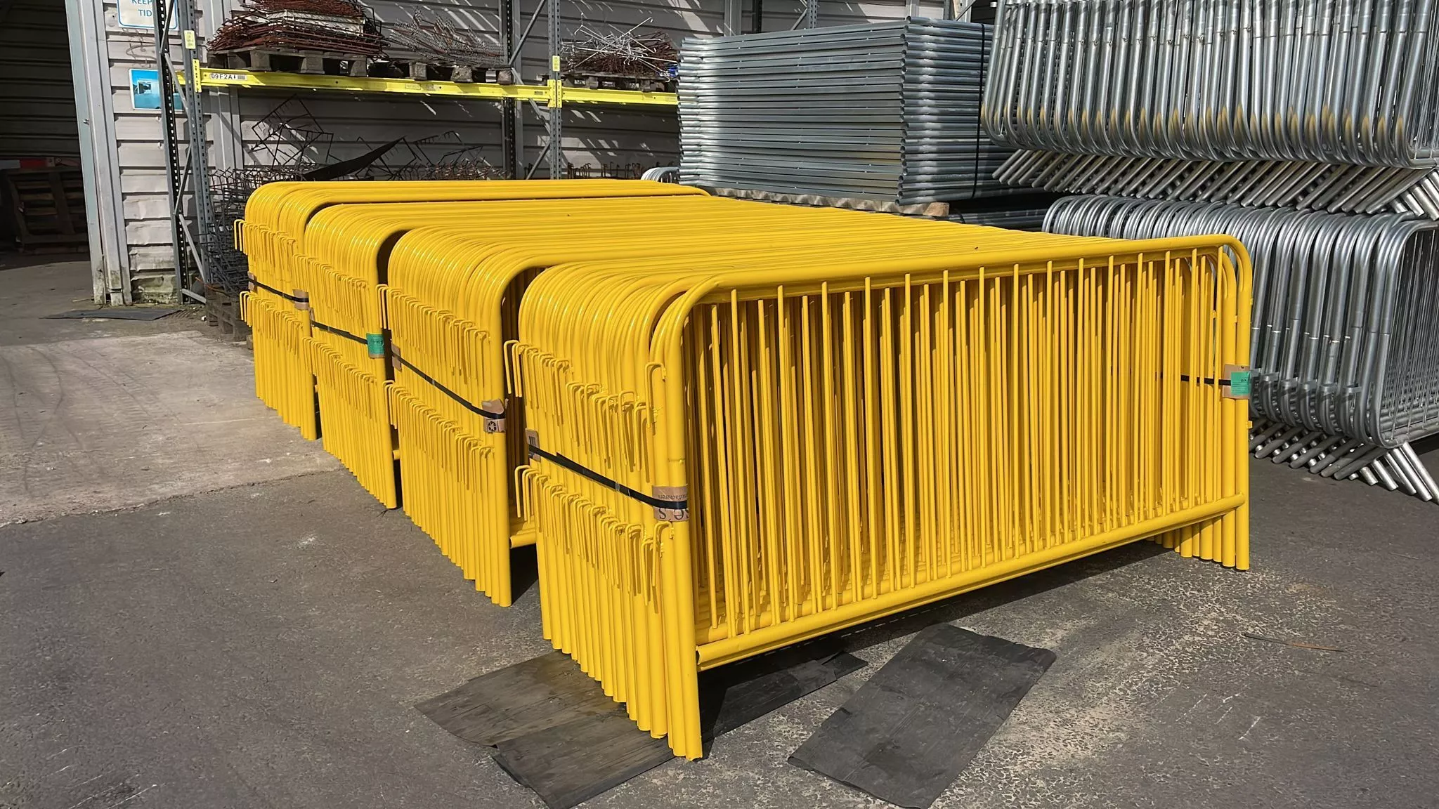 A large stack of vibrant yellow and durable galvanized Crowd Control Barriers for Events & Public Safety, showcasing DB Fencing's extensive stock ready for B2B distribution. These hot-dipped galvanized barriers are ideal for event management and public safety, meeting strict compliance standards for export to Australia, New Zealand, and global markets.