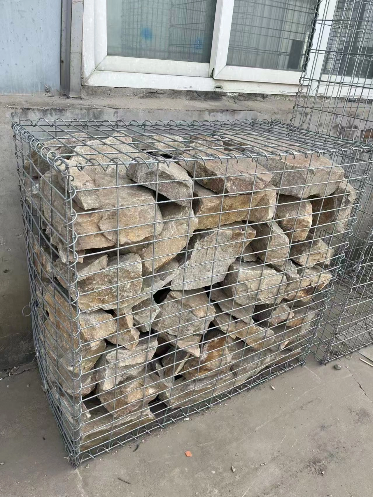 Heavy-duty galvanized gabion cage filled with stone, functioning as a robust Hesco Barrier for civil engineering and construction site security by DB Fencing.