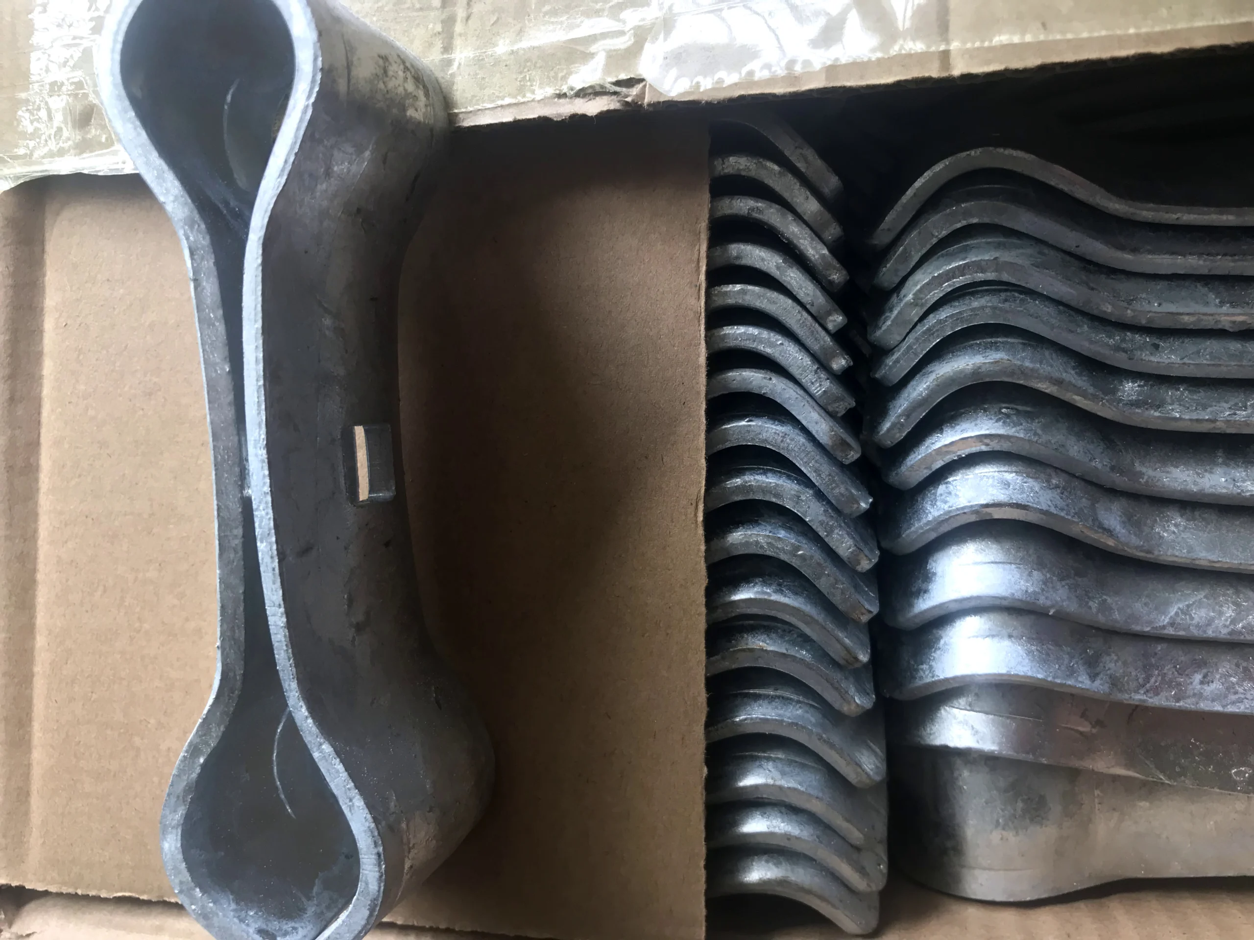 A close-up view of multiple heavy-duty galvanized temporary fence feet and base systems, neatly stacked and ready for shipment in a cardboard box. These durable components are manufactured by DB Fencing for secure temporary fencing installations on construction sites and events, adhering to high compliance standards for global export.