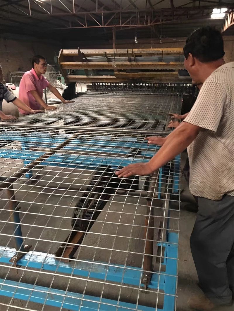 DB Fencing factory workers assemble Hesco Barriers on a high-capacity welding line in Anping. These galvanized wire mesh structures are designed for robust construction site security and flood control applications.