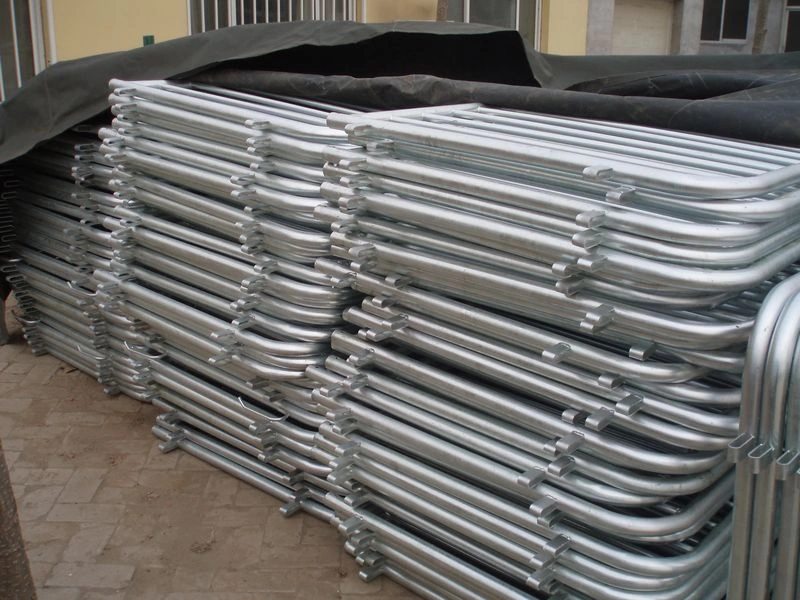 A large inventory of hot-dipped galvanized crowd control barriers, featuring durable tubular construction with rounded tops and integrated connection hooks, stacked and ready for shipment from DB Fencing. These high-quality barriers are designed for effective event perimeter management and public safety, demonstrating DB Fencing's commitment to robust and compliant products for global markets.