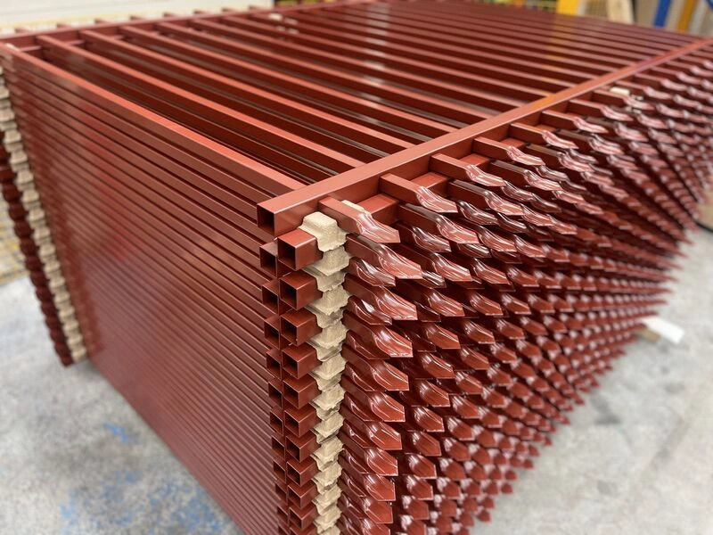 Stacks of reddish-brown hot-dipped galvanized steel picket fencing manufactured by DB Fencing. This temporary fence solution features durable square tubes and a secure welded base plate for construction sites and events.