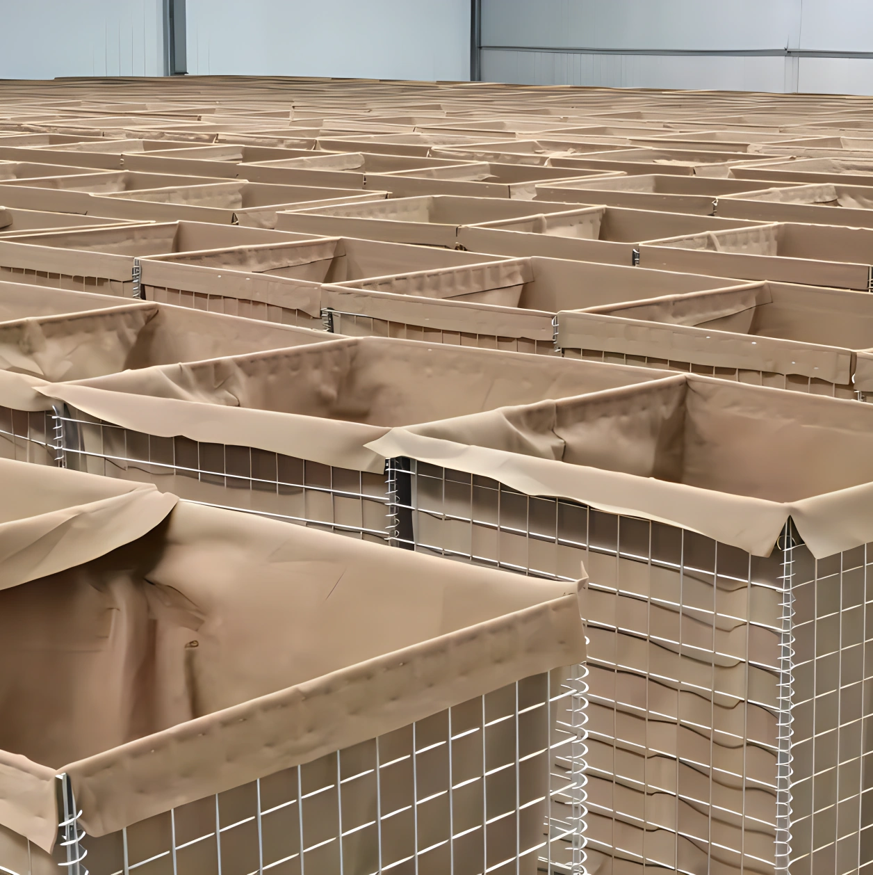 Rows of heavy-duty Hesco barriers featuring galvanized wire mesh and protective liners. Manufactured by DB Fencing, these units provide secure temporary containment for civil engineering and construction projects.