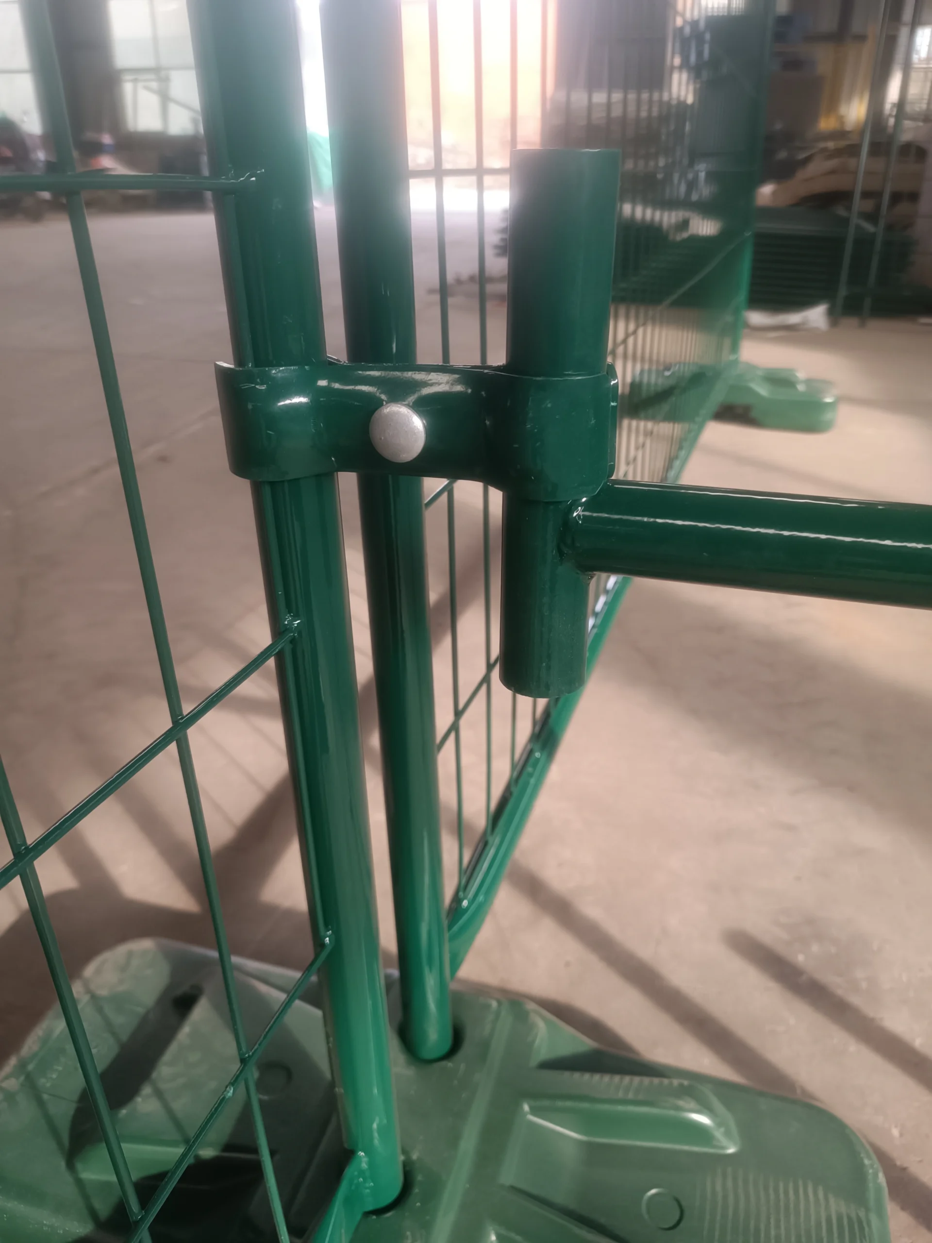 Close-up of a green temporary fence panel showing a secure clamp connection to another post, with the panel firmly seated in a durable green plastic base, illustrating our robust Temporary Fence Feet & Base Systems. As a leading manufacturer, DB Fencing produces these hot-dipped galvanized systems, including proprietary plastic feet, meeting Australian Standard AS 4687 for construction sites and events.