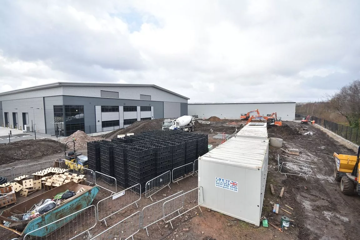 A dynamic construction site view featuring prominent stacks of black temporary fence feet and base systems, essential for securing the perimeter. This image highlights DB Fencing's capability in supplying high-quality temporary fence components for large-scale construction and civil engineering projects, leveraging our expertise in manufacturing durable base systems.