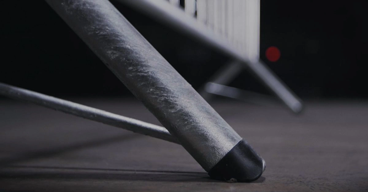 A close-up of a galvanized steel temporary fence leg, fitted with a black plastic foot cap, resting on a concrete surface. This image highlights DB Fencing's high-quality temporary fence feet & base systems, demonstrating our specialized manufacturing capabilities, including our own plastic feet machine, for superior stability and product longevity.