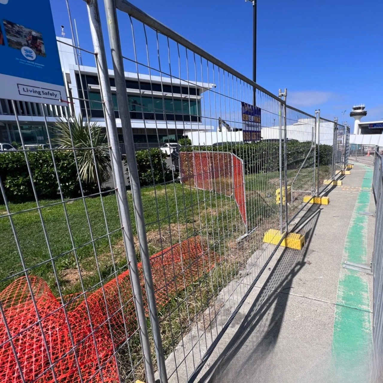Durable temporary fencing systems from DB Fencing securing a construction site near an airport building, featuring high-quality wire mesh panels and our unique yellow plastic temporary fence feet & base systems. These AS 4687-2022 compliant temporary fencing solutions provide essential perimeter security for construction and civil engineering projects, reflecting DB Fencing's commitment to safety and quality.