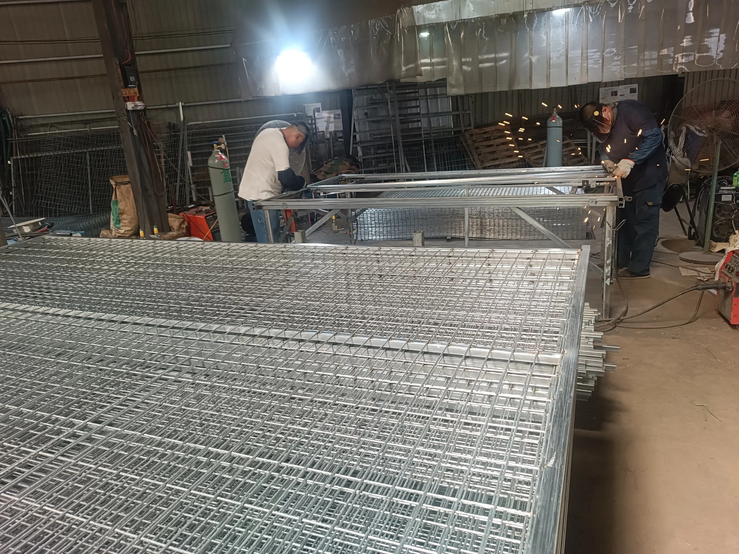Factory workers assembling galvanised temporary fencing panels on a high-volume production line