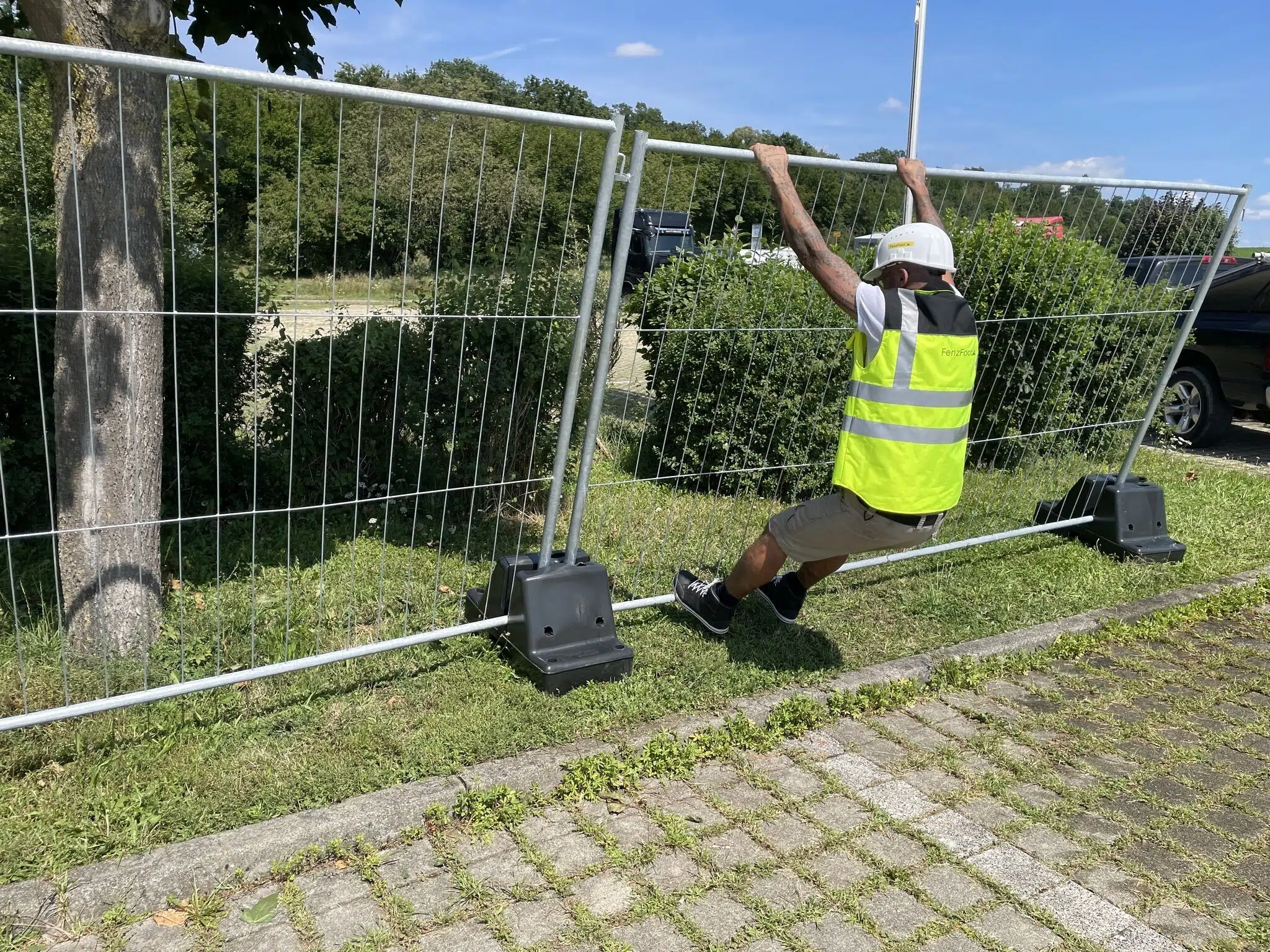 A construction worker in a high-visibility vest and hard hat tests the strength of DB Fencing's temporary fencing systems for construction sites, hanging from a robust wire mesh panel. This highlights the superior durability and stable support from our proprietary plastic fence feet, ensuring reliable site security and compliance with AS 4687 standards.